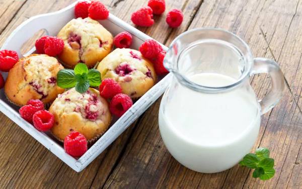 4K Ultra HD wallpaper featuring fresh raspberry muffins with scattered berries and a glass pitcher of milk on a rustic wooden table.