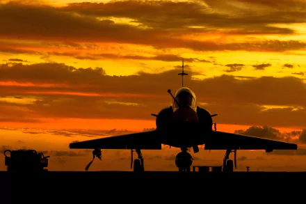 Silhouette of a Dassault Mirage 2000 jet fighter on the ground against an orange sky at sunset, captured in an HD military aircraft wallpaper.
