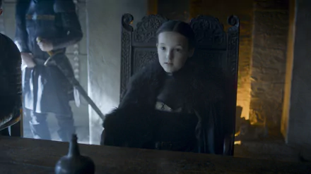 HD desktop wallpaper featuring Bella Ramsey as Lyanna Mormont from the TV show Game of Thrones, seated in a dark, medieval setting.