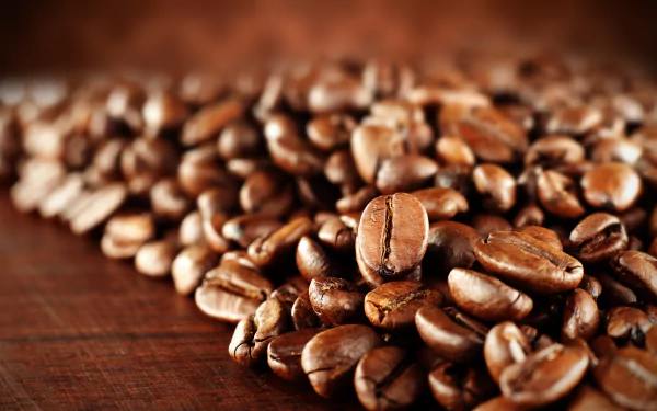 A close-up of rich, roasted coffee beans scattered on a wooden surface, showcasing their deep brown hues. This vibrant image serves as a 4K Ultra HD desktop wallpaper.