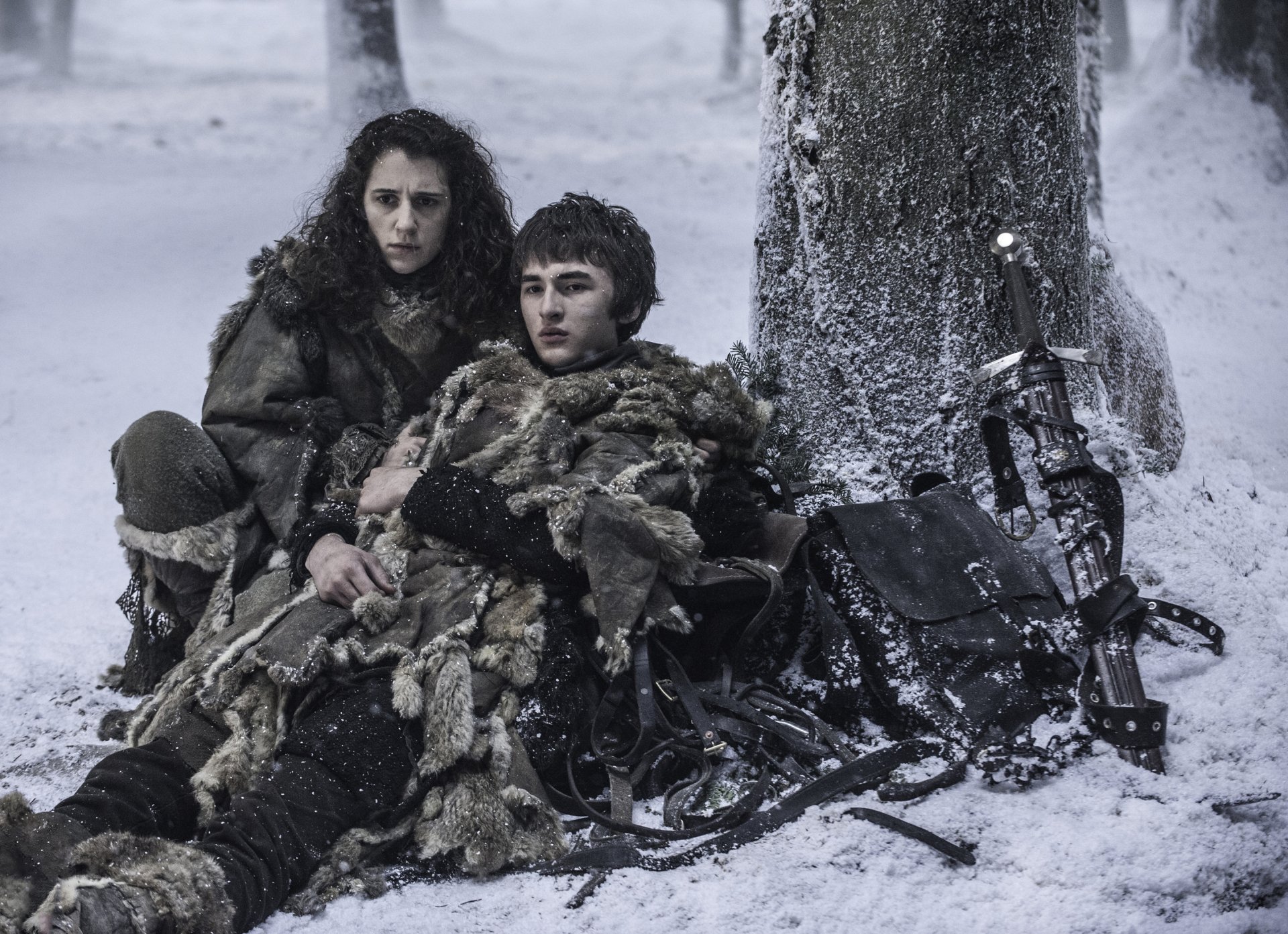 Bran Stark and Meera Reed, portrayed by Isaac Hempstead-Wright and Ellie Kendrick in Game of Thrones, rest against a snowy tree in this HD desktop wallpaper.