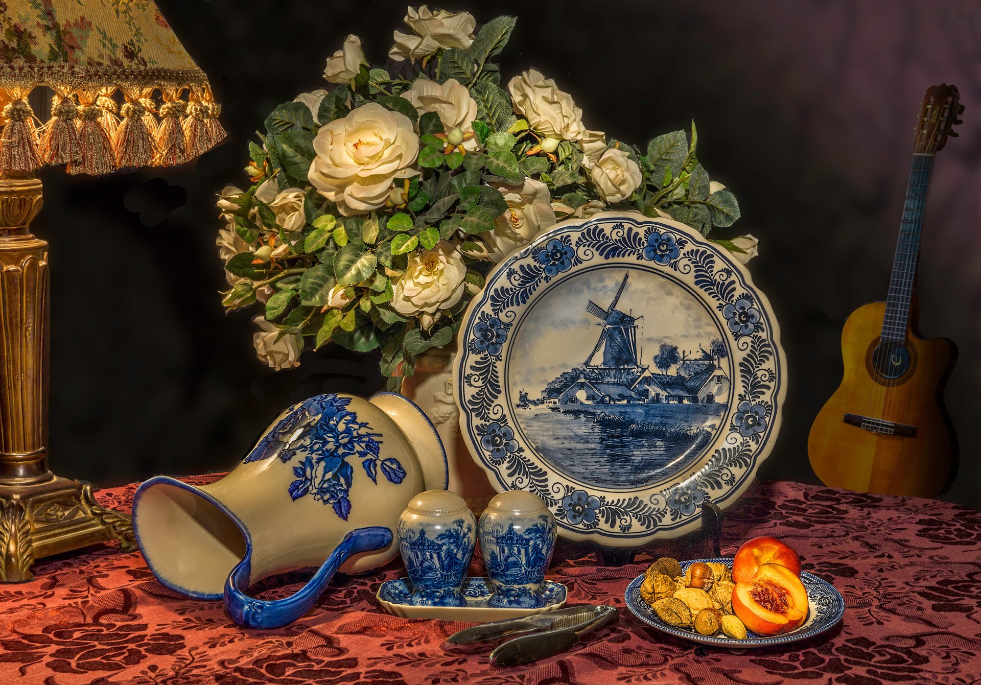A captivating still life featuring a guitar, a lamp, vibrant fruit, a decorative pitcher, a plate with a ship design, and roses, creating a warm and artistic atmosphere.