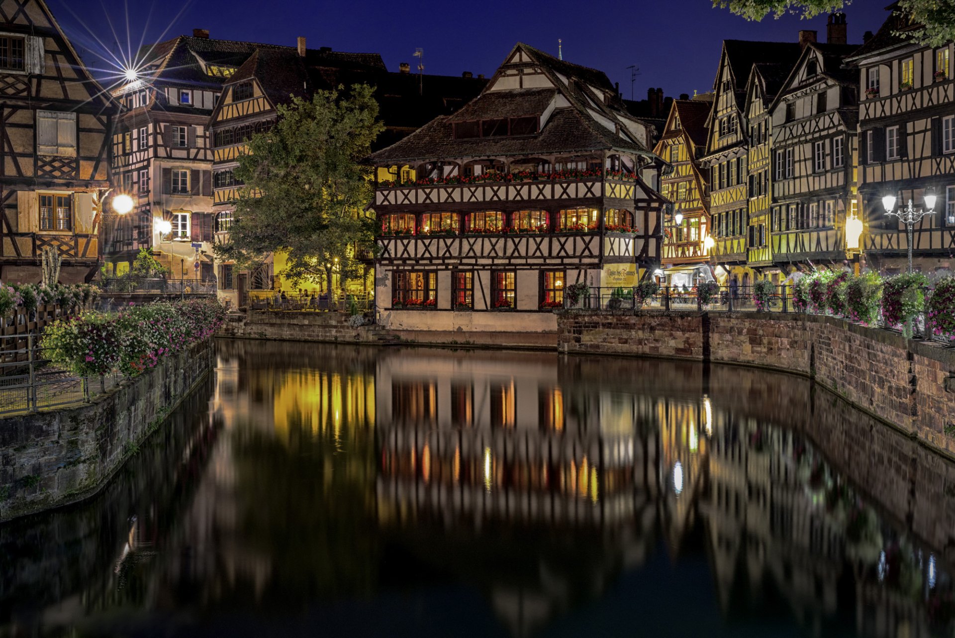 Night view of illuminated historic buildings reflecting on a canal in Strasbourg, France, creating a serene cityscape for an HD desktop wallpaper.