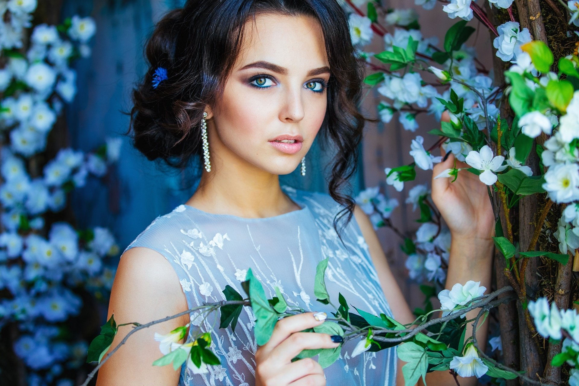 A woman posing amidst blooming flowers in an HD desktop wallpaper and background. She exudes elegance with her styled hair and dangling earrings.