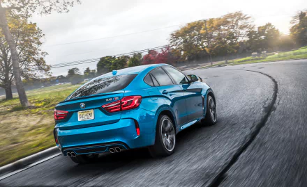 Blue BMW X6 SUV driving on a curved road with autumn trees in the background, featured as an HD PC desktop wallpaper and background.