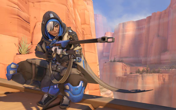 Ana (Overwatch) crouched on a canyon ledge aiming her sniper rifle — HD video game desktop wallpaper/background with warm desert cliffs.