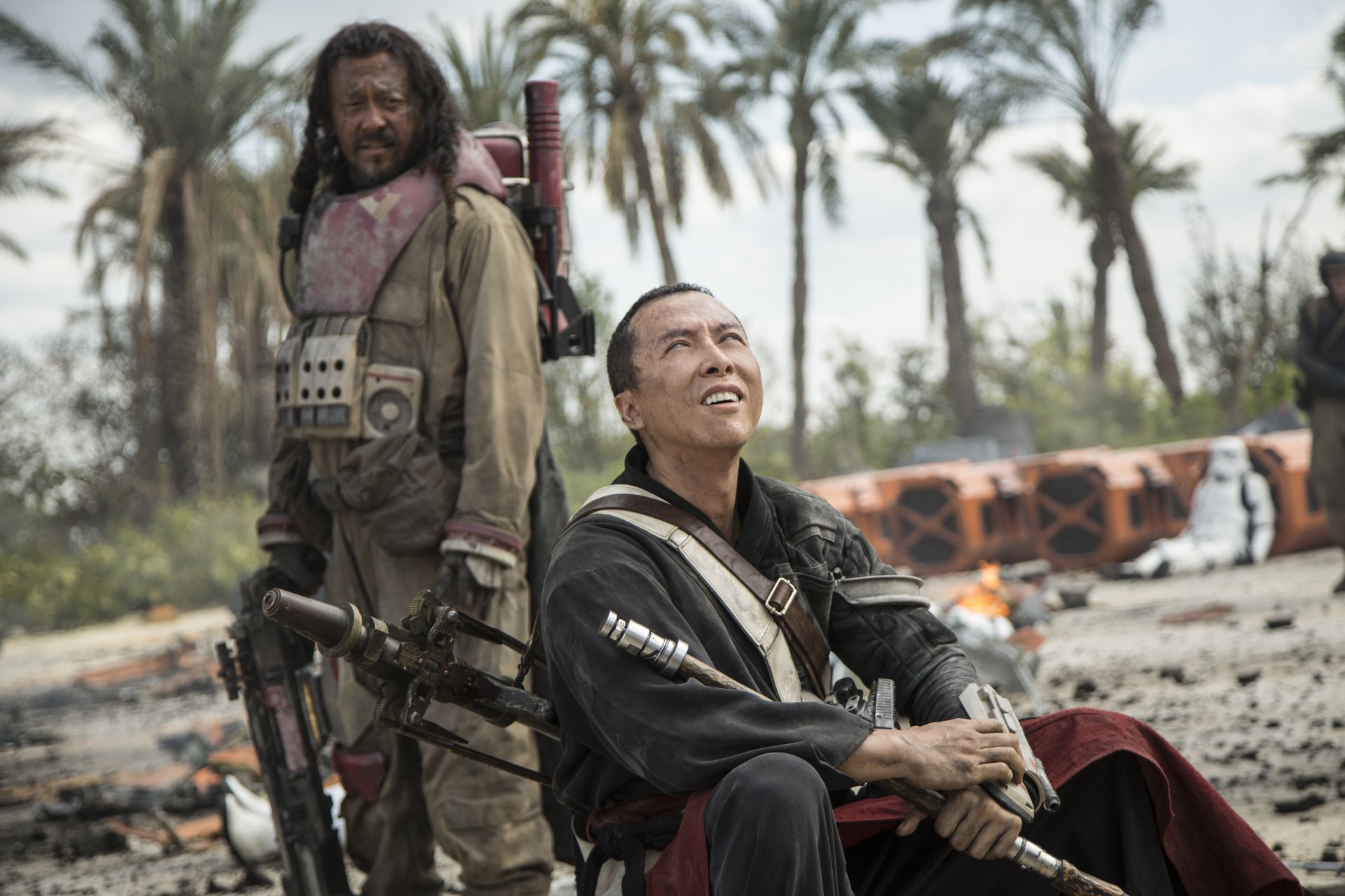 A captivating HD wallpaper featuring Baze Malbus and Chirrut Îmwe from Rogue One: A Star Wars Story, set against a backdrop of palm trees and debris.