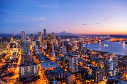 4K Ultra HD night cityscape of Seattle, USA, featuring illuminated skyscrapers and buildings along the waterfront under a clear twilight sky.