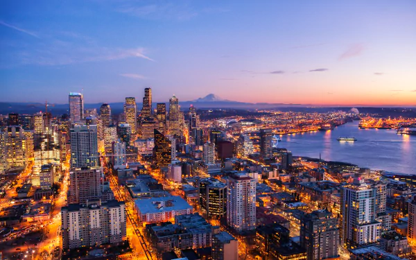 4K Ultra HD night cityscape of Seattle, USA, featuring illuminated skyscrapers and buildings along the waterfront under a clear twilight sky.