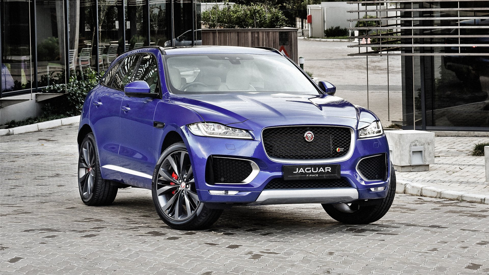 Blue Jaguar F-PACE SUV parked on a paved street, showcased as a high-definition desktop wallpaper featuring the sleek design of this luxury vehicle.
