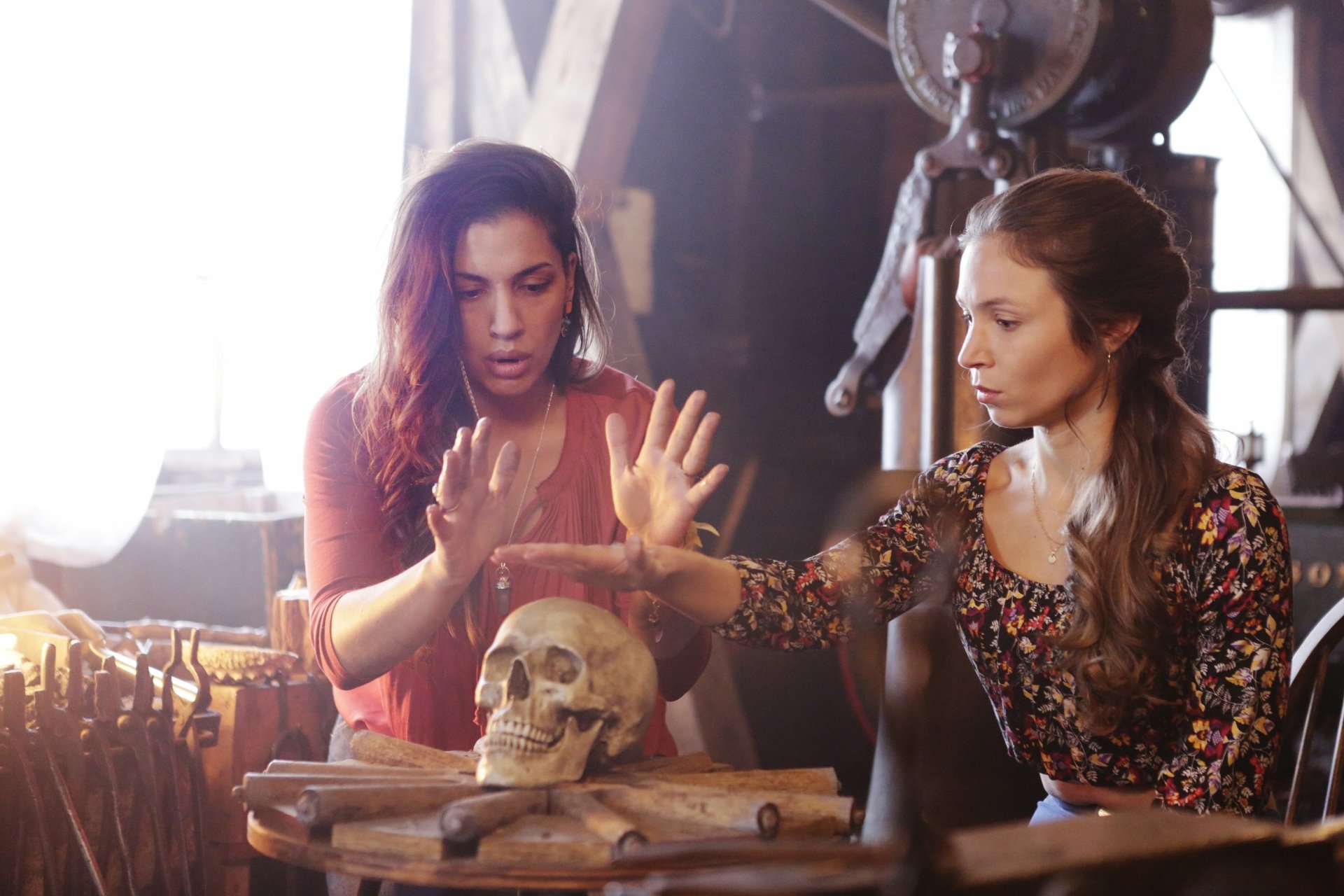 Wynonna Earp 2K Quad HD PC desktop wallpaper/background: two women examine a skull on a cluttered workbench, one raising her hands as if performing a ritual.