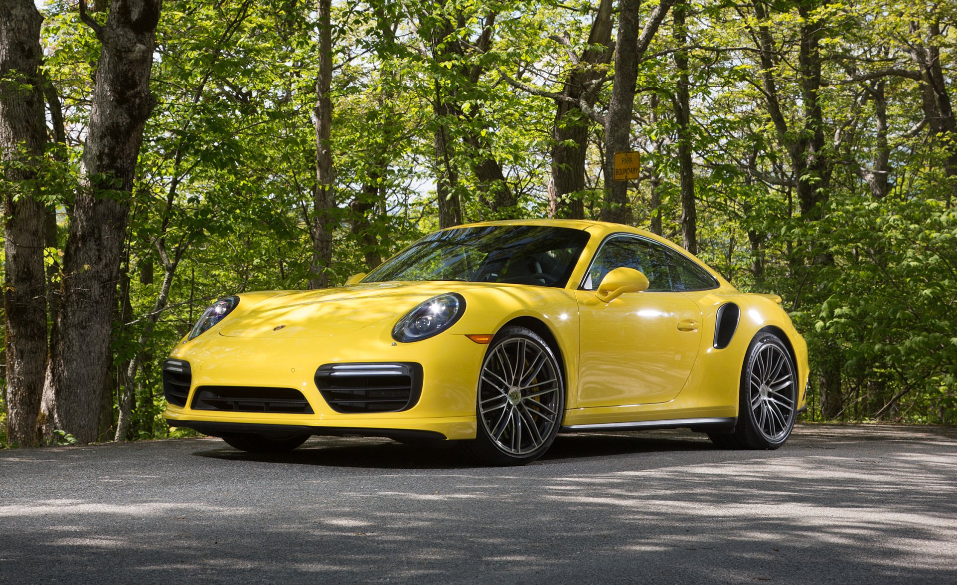 Yellow Porsche 911 Turbo parked on a forest road, showcasing sleek design and sporty features in this HD PC desktop wallpaper and background.