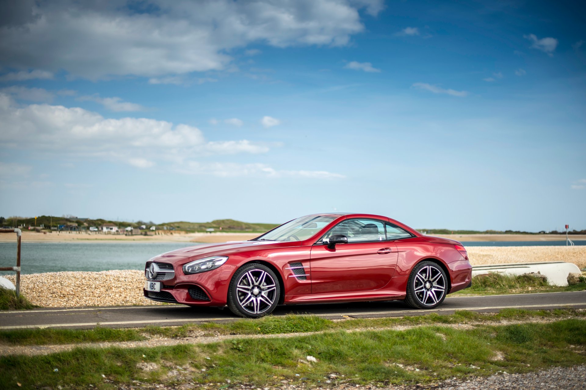 Red Mercedes-Benz SL-Class grand tourer vehicle parked by the seaside on a clear day — 4K Ultra HD PC desktop wallpaper and background.
