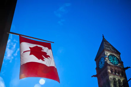 HD desktop wallpaper featuring a Canadian flag waving beside a historic clock tower in Toronto against a clear blue sky.