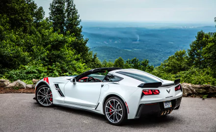 White Chevrolet Corvette (C7) sports car parked by a scenic overlook with lush greenery and a distant mountain view, captured in HD for a desktop wallpaper.
