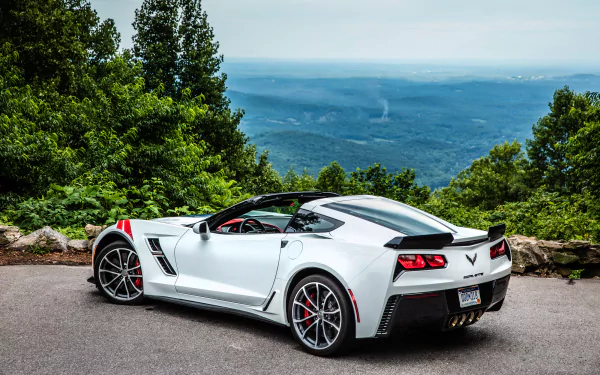 White Chevrolet Corvette (C7) sports car parked by a scenic overlook with lush greenery and a distant mountain view, captured in HD for a desktop wallpaper.