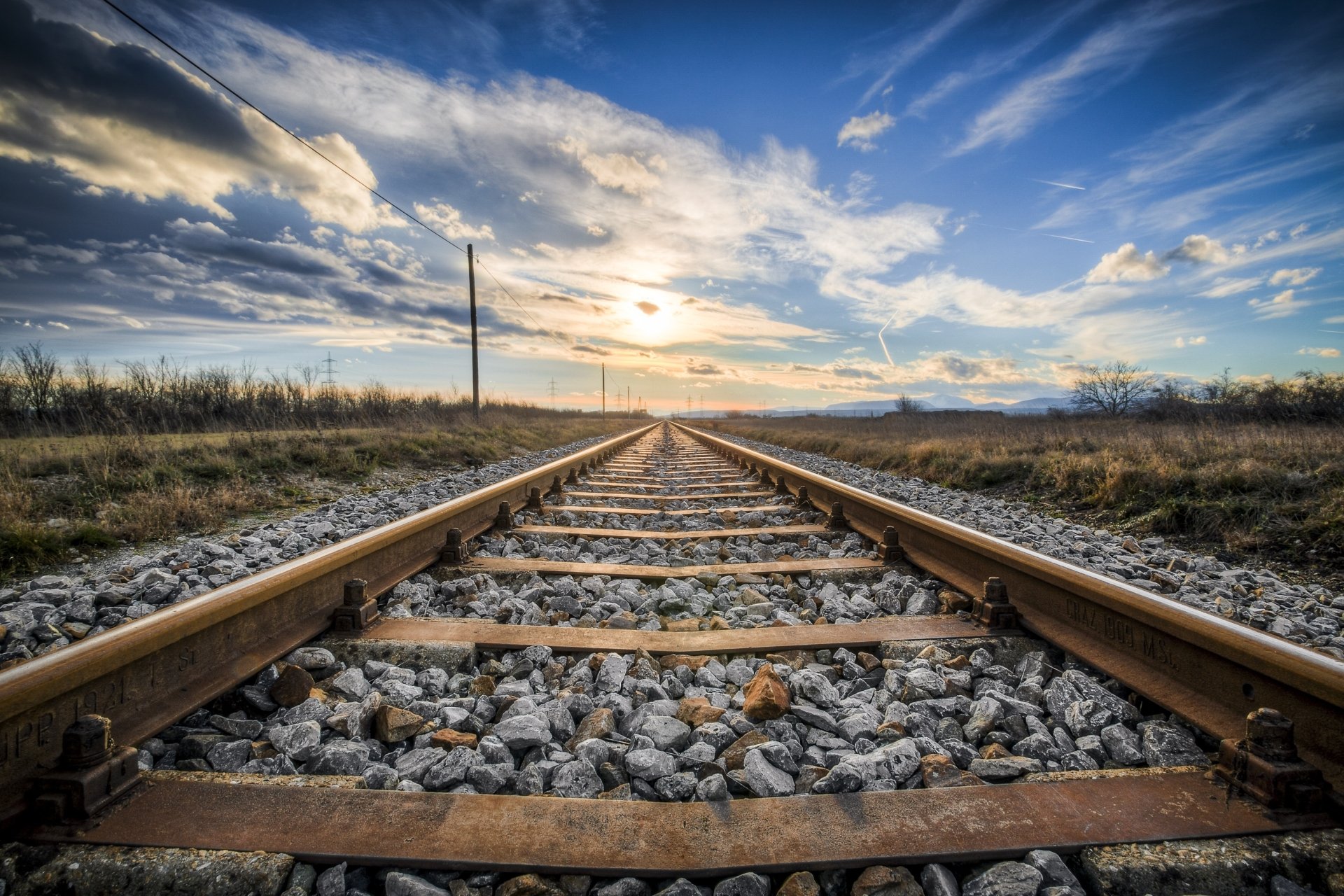 HD desktop wallpaper showcasing a man-made railroad stretching into the horizon under a vibrant sky with scattered clouds.