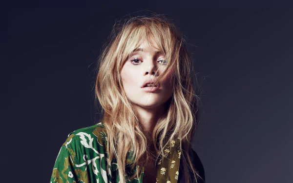 HD desktop wallpaper portrait of a blonde model with brown eyes wearing a patterned green top against a dark studio backdrop.