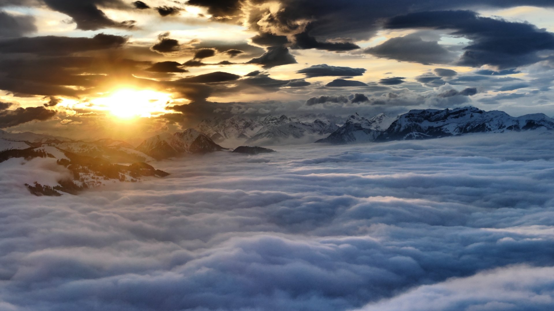 A sunset casts golden light over undulating clouds and majestic mountains in Austria, captured in this stunning aerial view evoking the beauty of nature.