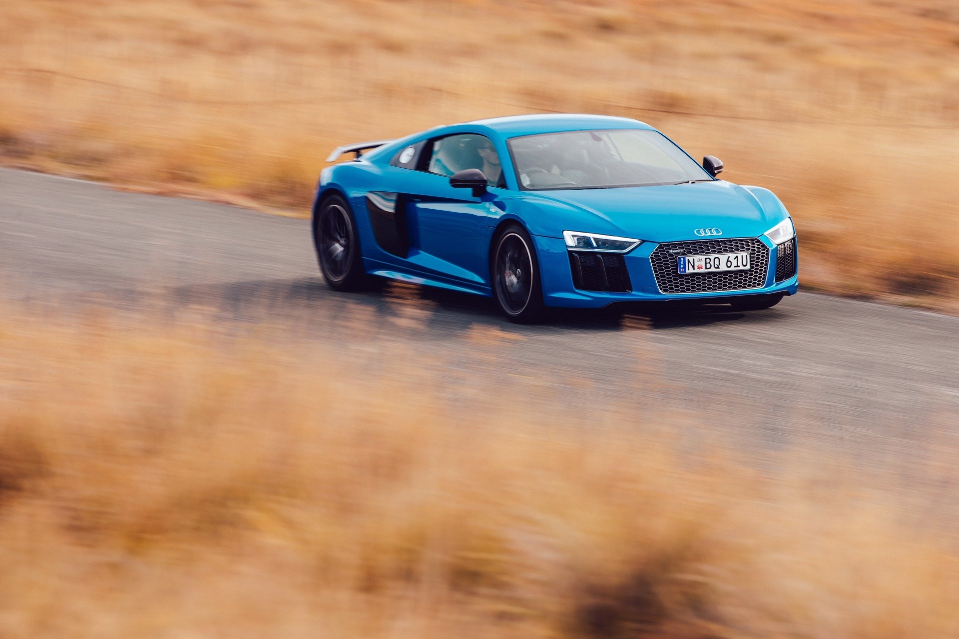 Blue Audi R8 V10 supercar speeding on a winding road, captured in a sharp 4K Ultra HD desktop wallpaper showcasing the sleek vehicle in motion.