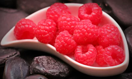 Vivid raspberries in a white curved bowl on dark stones — fruit, berry food close-up; 4K Ultra HD PC desktop wallpaper background.