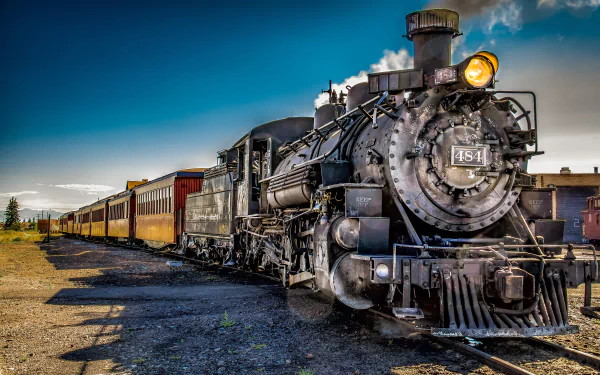 A detailed steam locomotive is positioned prominently in this 4K Ultra HD wallpaper, showcasing its vintage design alongside a series of passenger carriages against a bright blue sky.