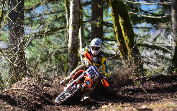 A motocross rider on a KTM motorcycle speeds through a dense forest trail, captured in vivid detail for an HD PC desktop wallpaper background.