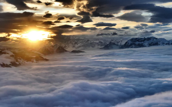 A sunset casts golden light over undulating clouds and majestic mountains in Austria, captured in this stunning aerial view evoking the beauty of nature.