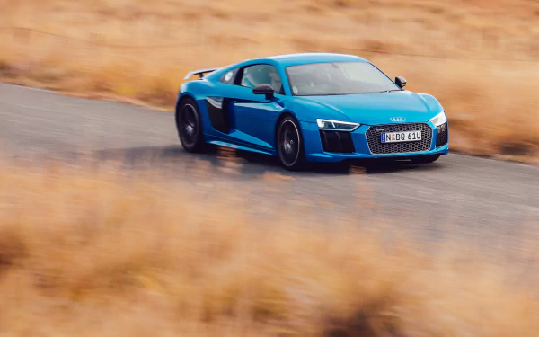 Blue Audi R8 V10 supercar speeding on a winding road, captured in a sharp 4K Ultra HD desktop wallpaper showcasing the sleek vehicle in motion.