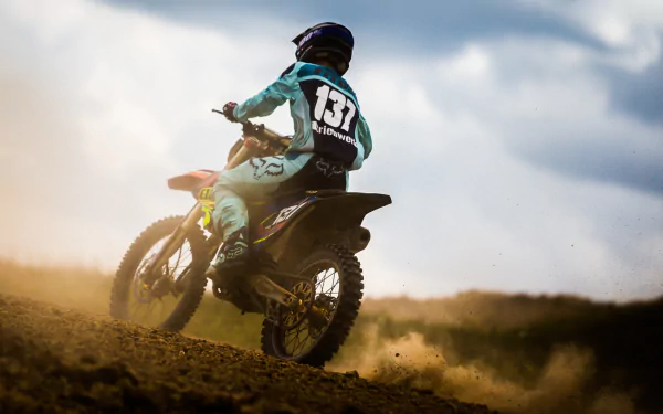 A motocross rider navigates a dirt track, kicking up dust in a dynamic action shot. The image captures the thrill of dirt biking, making it a striking HD desktop wallpaper.
