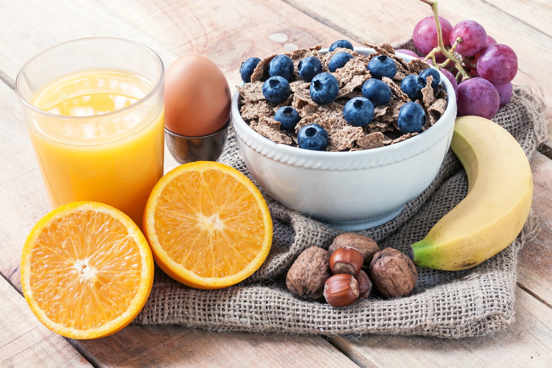 A vibrant 4K Ultra HD desktop wallpaper showing a healthy breakfast spread with muesli topped with blueberries, grapes, banana, nuts, an egg, and a glass of orange juice.