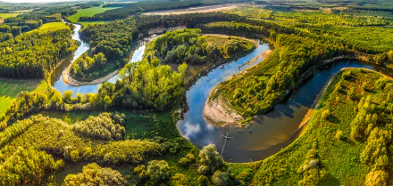 Aerial view of a winding river meandering through lush forests in the Czech Republic, showcasing vibrant nature and a stunning landscape. High-definition image for desktop backgrounds.