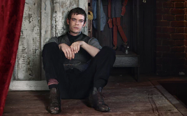 A character from the TV show Penny Dreadful sits against a wall, reflecting a moody atmosphere. This HD desktop wallpaper captures the show's dark aesthetic and emotional depth.