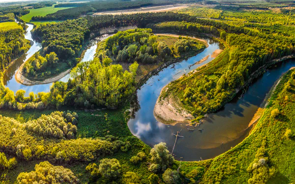 Aerial view of a winding river meandering through lush forests in the Czech Republic, showcasing vibrant nature and a stunning landscape. High-definition image for desktop backgrounds.