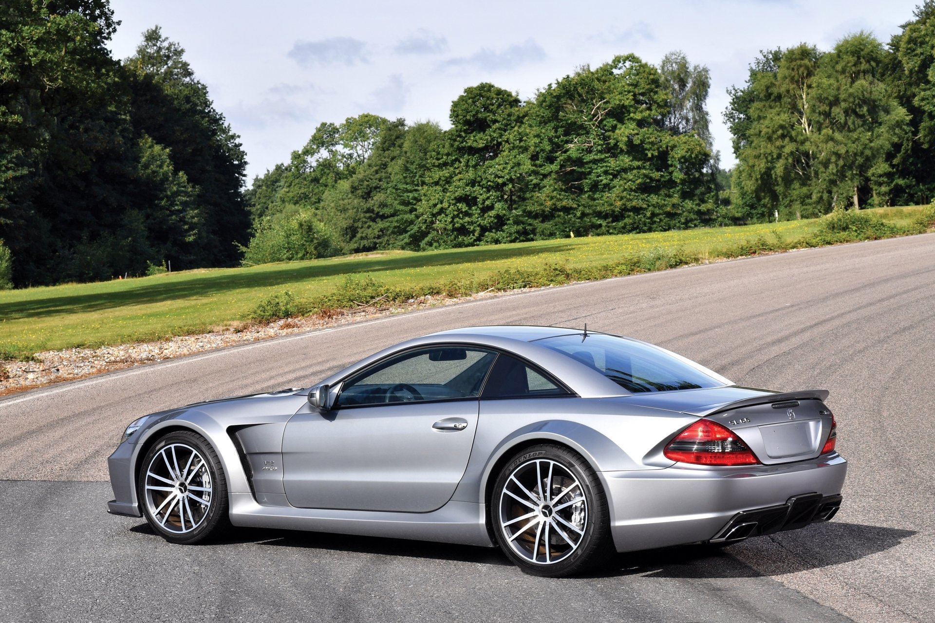 Silver Mercedes-Benz SL-Class grand tourer parked on a curved road with lush green trees in the background, captured in 4K Ultra HD for PC desktop wallpaper.