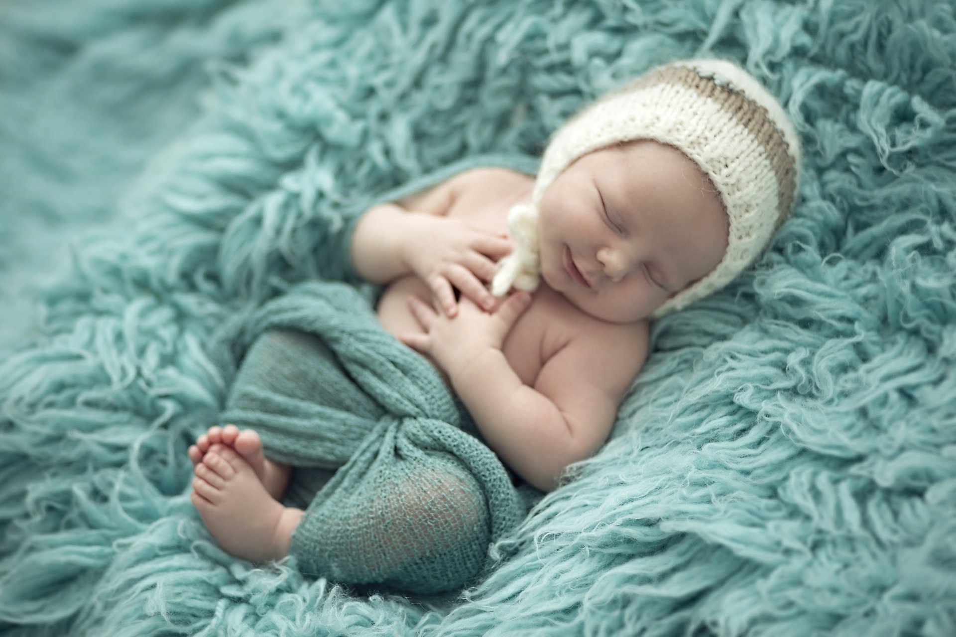 A cute baby peacefully sleeping and smiling on a soft, textured blue blanket, captured in high-definition photography for a charming PC desktop wallpaper.