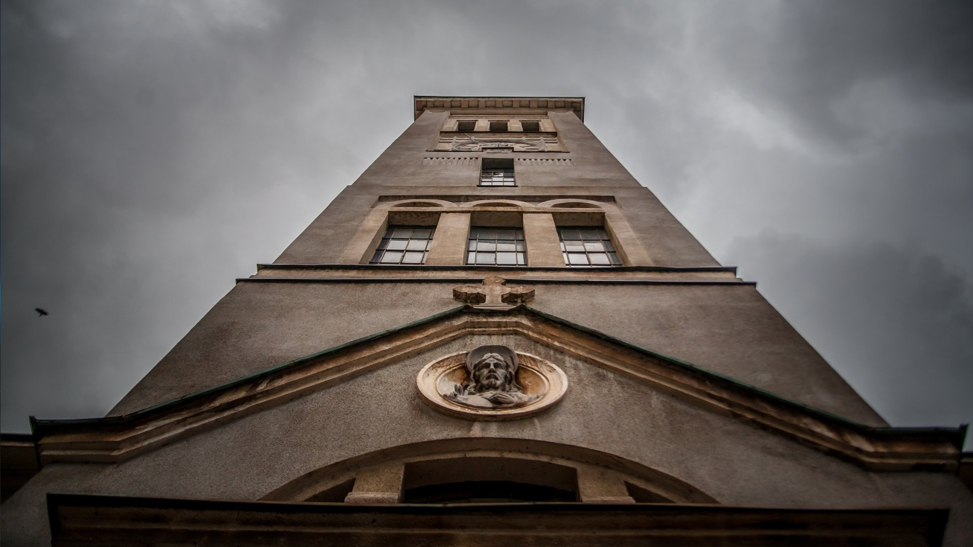 Low-angle view of Church of Saint-Pierre tower against a moody sky, religious stone facade with sculpted medallion — 2K Quad HD PC desktop wallpaper/background.