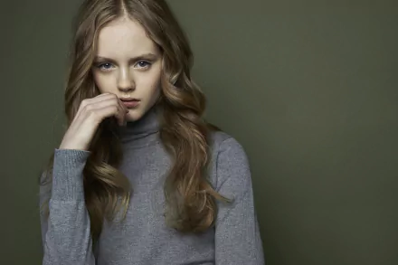 HD desktop wallpaper featuring brunette model Emma Laird with striking blue eyes, posing thoughtfully against a muted green background.