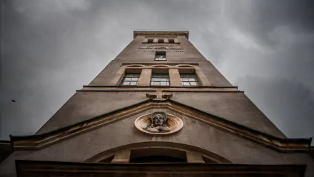 Low-angle view of Church of Saint-Pierre tower against a moody sky, religious stone facade with sculpted medallion — 2K Quad HD PC desktop wallpaper/background.