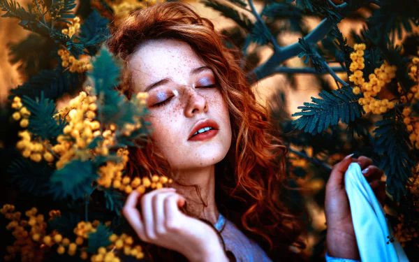 A serene redhead model with freckles closes her eyes, surrounded by vibrant yellow flowers, showcasing a mood of tranquility and beauty. Perfect for a high-definition PC wallpaper.