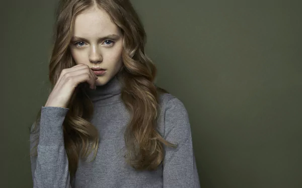 HD desktop wallpaper featuring brunette model Emma Laird with striking blue eyes, posing thoughtfully against a muted green background.