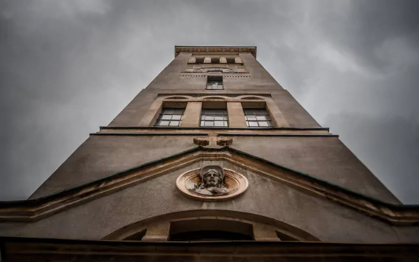 Low-angle view of Church of Saint-Pierre tower against a moody sky, religious stone facade with sculpted medallion — 2K Quad HD PC desktop wallpaper/background.