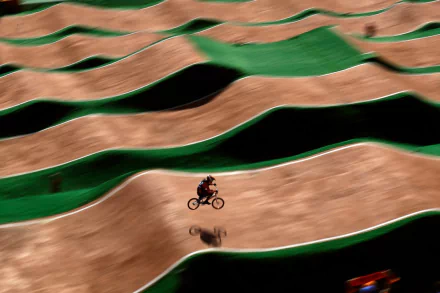 A BMX rider speeds across a track with dynamic, wavy terrain. This vibrant HD desktop wallpaper captures the thrill of sports in an energetic landscape.