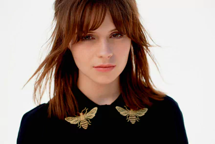 HD desktop wallpaper featuring a close-up of English singer Gabrielle Aplin with brunette hair and brown eyes, wearing a black top adorned with embroidered bees.
