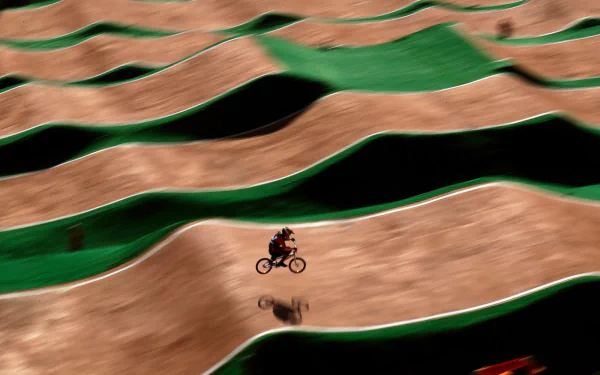 A BMX rider speeds across a track with dynamic, wavy terrain. This vibrant HD desktop wallpaper captures the thrill of sports in an energetic landscape.