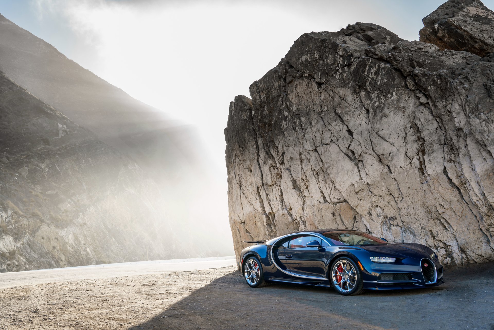 A stunning Bugatti Chiron parked against a dramatic rocky backdrop, showcasing its sleek design in a captivating 4K Ultra HD wallpaper for automotive enthusiasts.