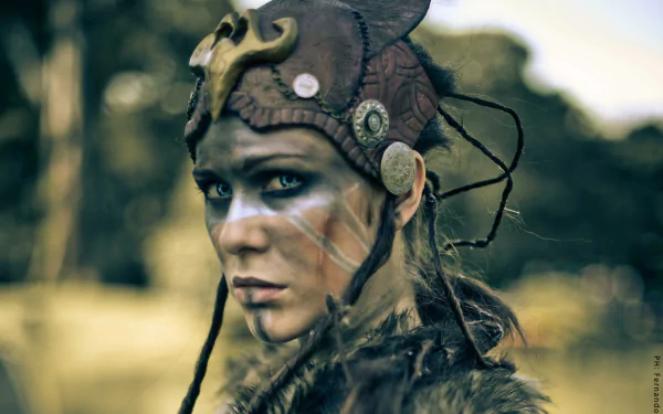 A striking cosplay of Senua from Hellblade: Senua's Sacrifice, showcasing intricate details in her costume and makeup, set against a blurred outdoor background. 4K Ultra HD quality.