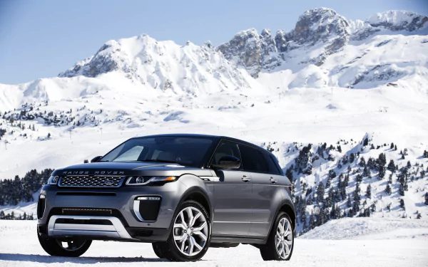 A silver Range Rover Evoque SUV parked on snowy terrain with snow-covered mountains in the background, captured in 4K Ultra HD quality.