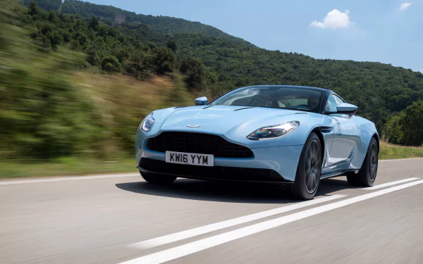 A sleek Aston Martin DB11 grand tourer cruising on a scenic road, captured in stunning 4K Ultra HD for a dynamic PC desktop wallpaper.