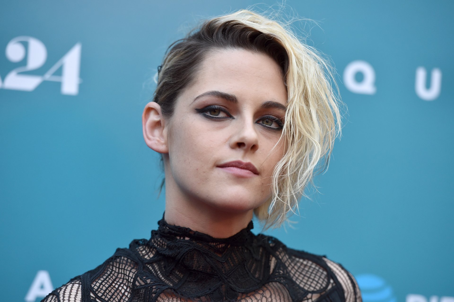 Kristen Stewart poses confidently against a vibrant blue backdrop. Her edgy hairstyle and striking eye makeup create a captivating look, making it a stunning HD desktop wallpaper.